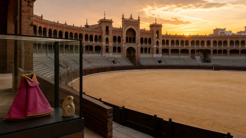 Plaza de toros genérica y vacía al atardecer con una vitrina cultural en primer plano