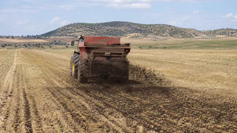 Máquina agrícola genérica esparciendo una enmienda orgánica sobre un campo de secano