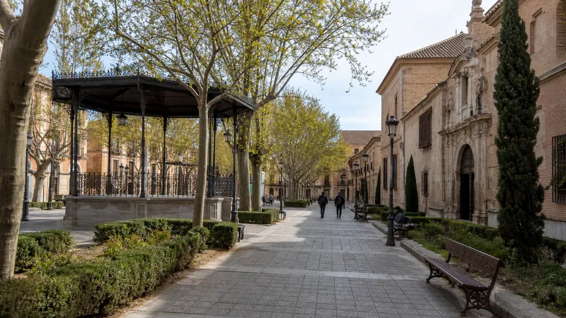 Plaza histórica arbolada de Alcalá de Henares con quiosco de música y fachadas castellanas