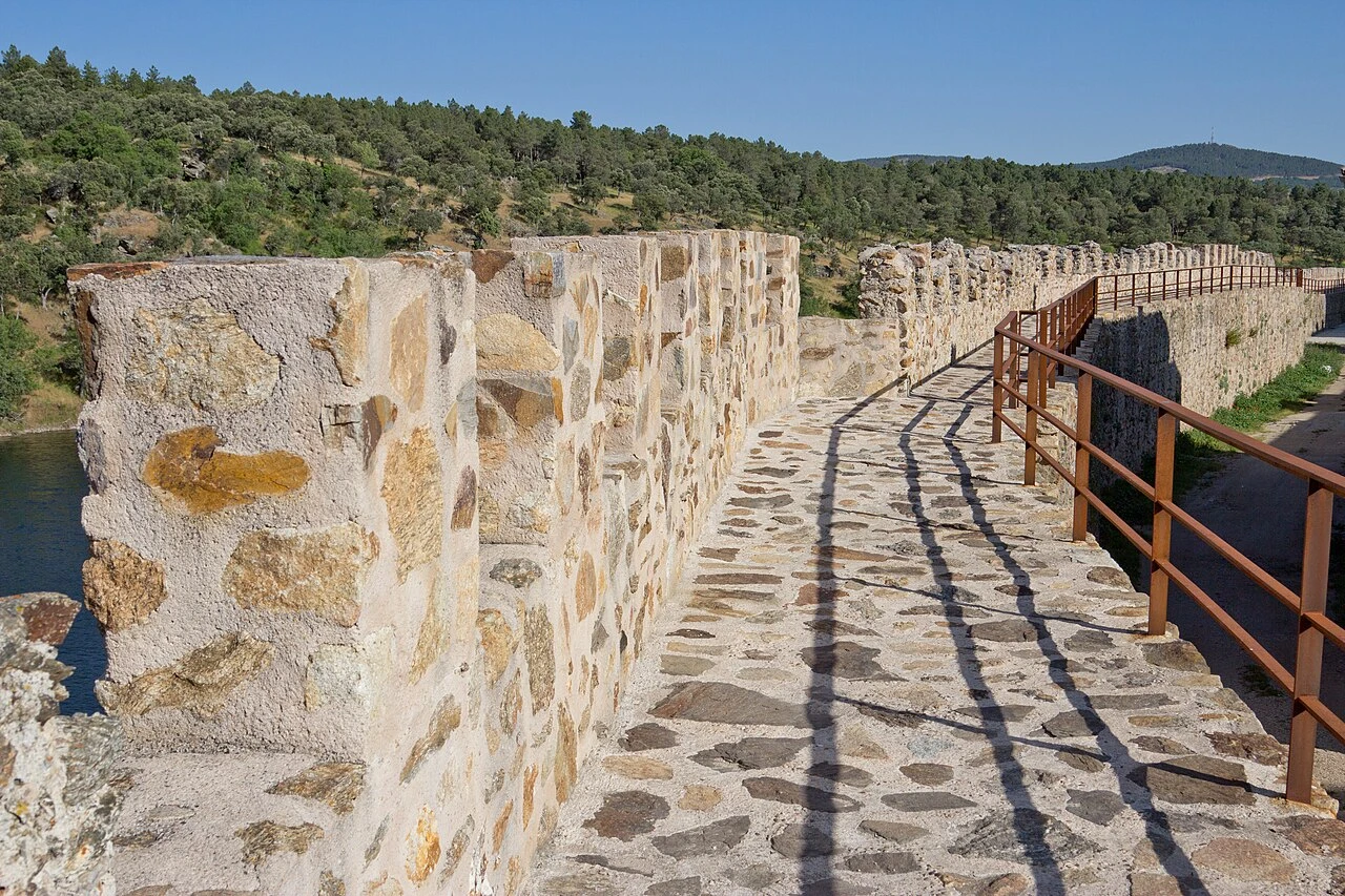 Camino de piedra del adarve bajo con almenas y barandilla junto al Lozoya