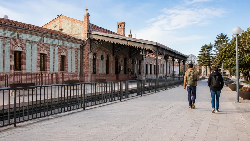 Viajeros caminando junto a una estación histórica de ladrillo de Aranjuez