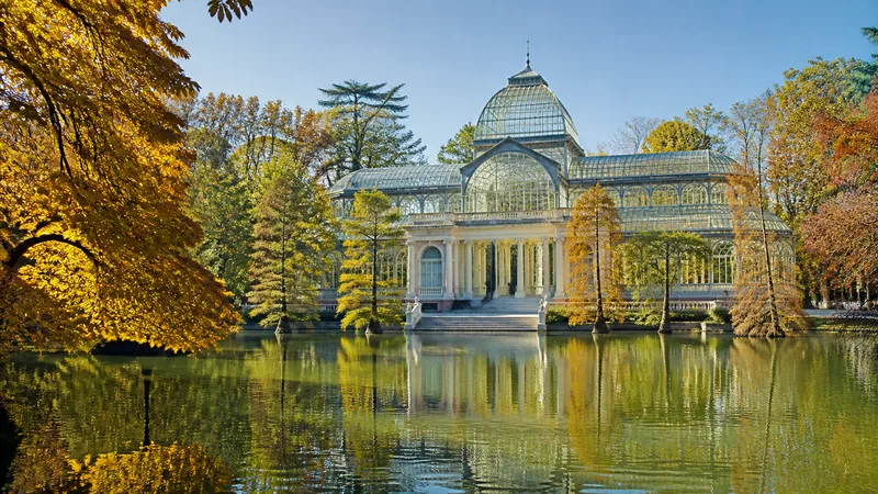 Palacio de Cristal reflejado en su estanque entre árboles