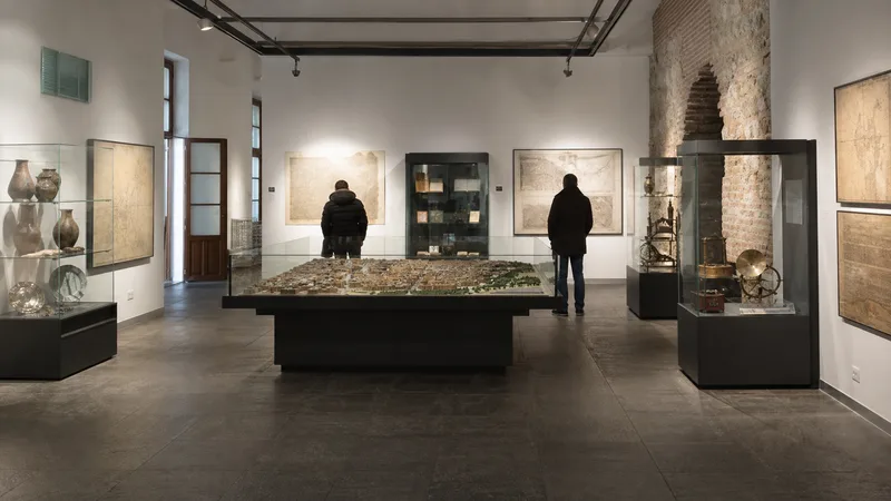Visitantes recorren un pequeño museo de historia con vitrinas y maqueta urbana