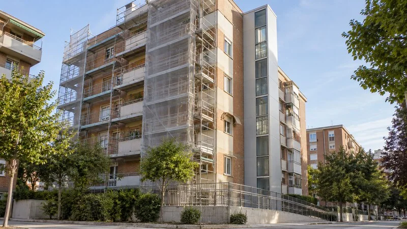 Bloque residencial en rehabilitación con andamio, ascensor exterior y rampa