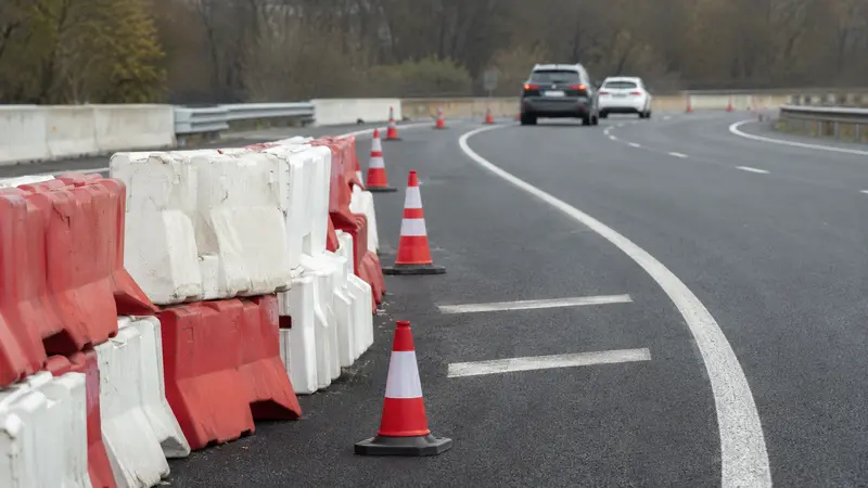 Barreras provisionales y conos junto a una calzada en obras con tráfico al fondo