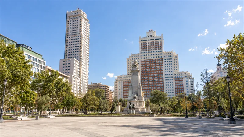 Vista diurna de la Plaza de España de Madrid con sus torres, vegetación y explanada peatonal.