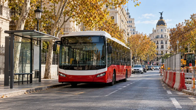 Autobús urbano rojo y blanco junto a una parada y barreras de obras en una calle de Madrid.